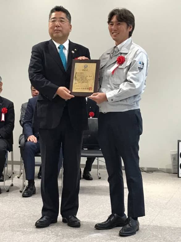 正装した男性が表彰状を持ちながら受賞者に手渡す瞬間