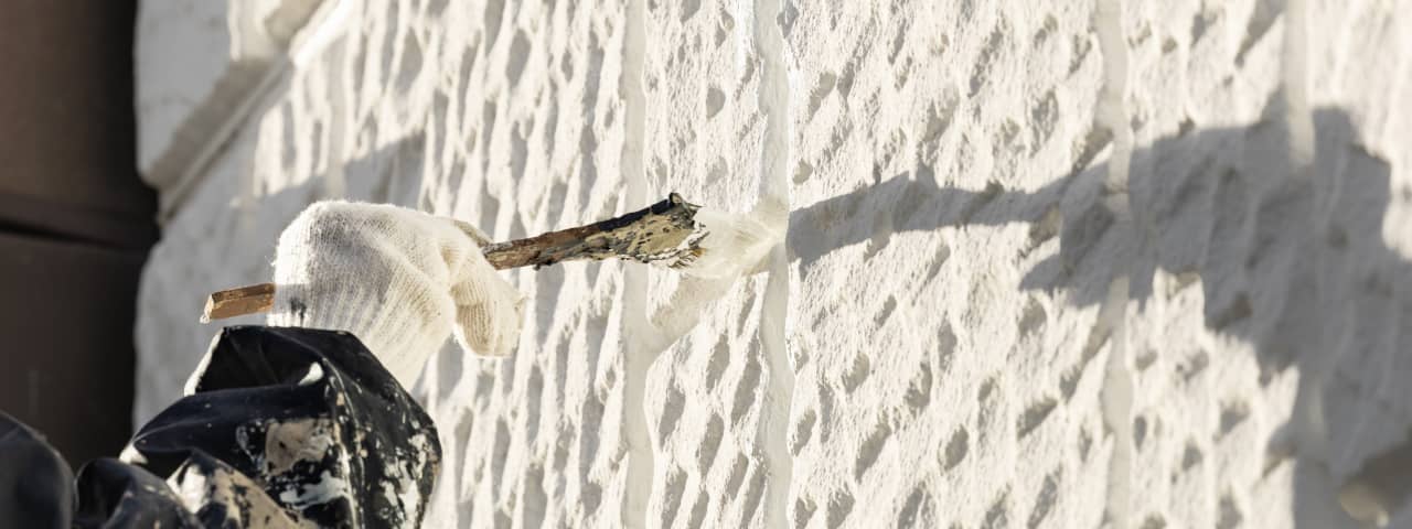 作業員が白い手袋を着用し、壁の凹凸部分にブラシで防水剤を塗布している様子