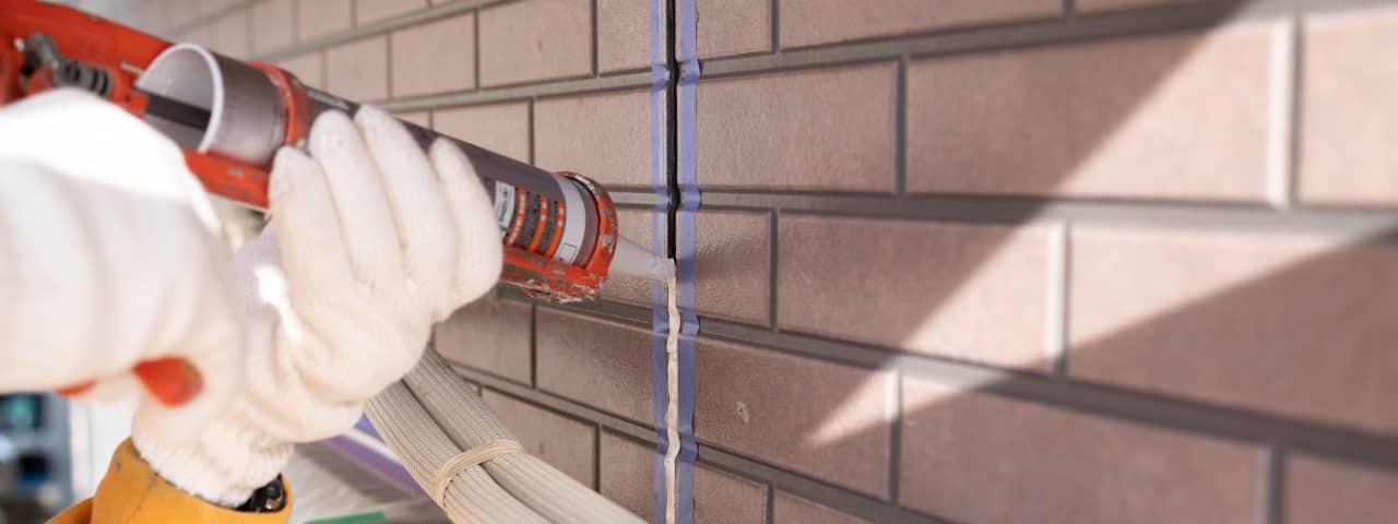 煉瓦の目地を補修中、白い手袋を着用した作業員が丁寧にシーリング材を注入している様子