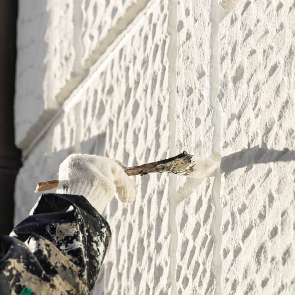  壁の凹凸部分に塗料を塗る作業員の手元。刷毛を使用して丁寧に塗装